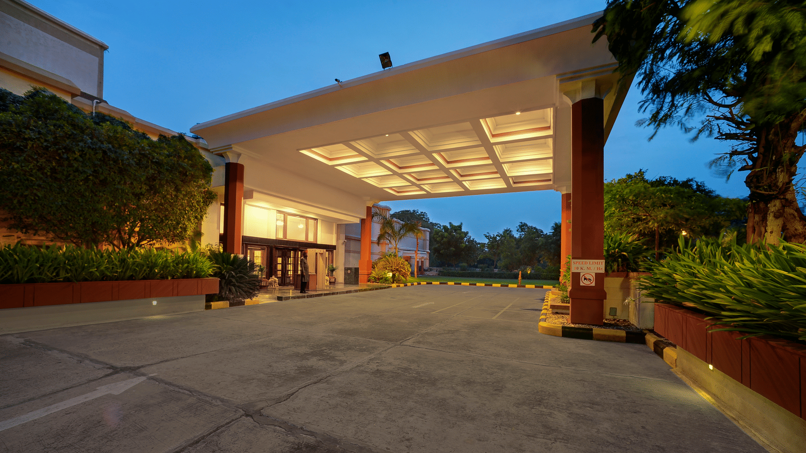 Entrance of The Ummed Ahmedabad hotel with landscaped driveway and evening lighting