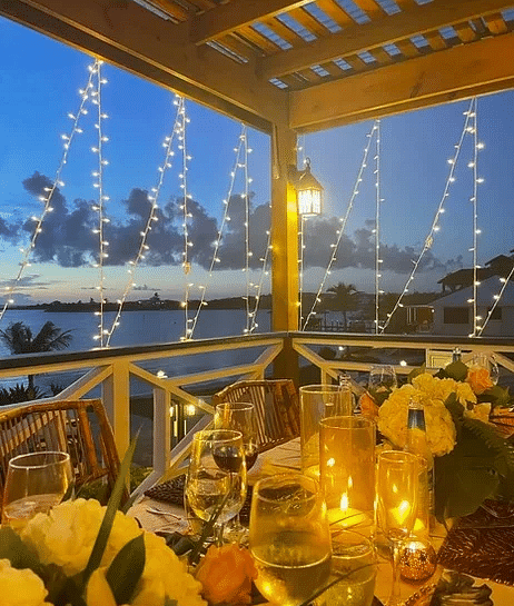 An outdoor dining table set under warm string lights at night, surrounded by tropical flowers and glowing lanterns | Abaco Inn