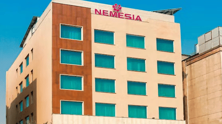 Daytime view of the Nemesia hotel building facade with teal-tinted windows, wooden accents, and palm trees in front.