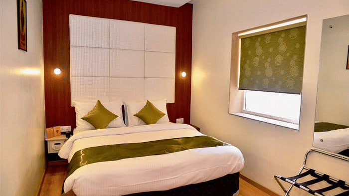 The Onyx double room with one large bed with pillows, an accent wall behind the bed, a window, and seating placed near the wall.