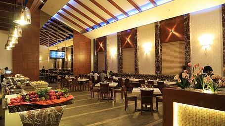 A sophisticated restaurant with an open buffet counter, stylish ceiling design, and ample seating. - Dhanalakshmi Srinivasan Hotels, Perambalur