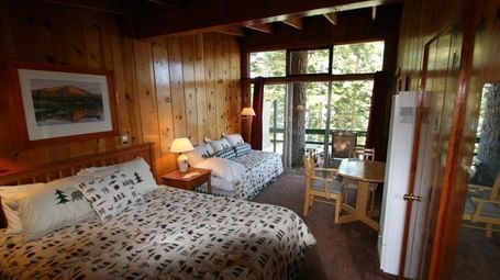 A cosy cabin room with two beds and patterned comforters, warm wood paneling, a framed picture. - Kit Carson Lodge & Restaurant