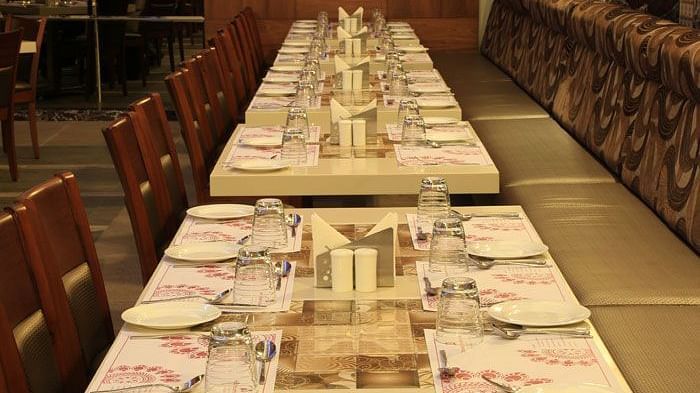 A long dining table set with fine cutlery and napkins, perfect for group dining and special occasions. - Dhanalakshmi Srinivasan Hotels, Perambalur