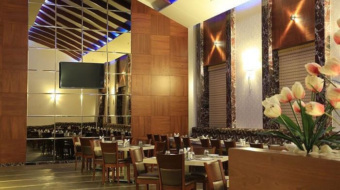 A grand dining area with high ceilings, wooden panel walls, and soft lighting for an upscale experience. - Dhanalakshmi Srinivasan Hotels, Perambalur