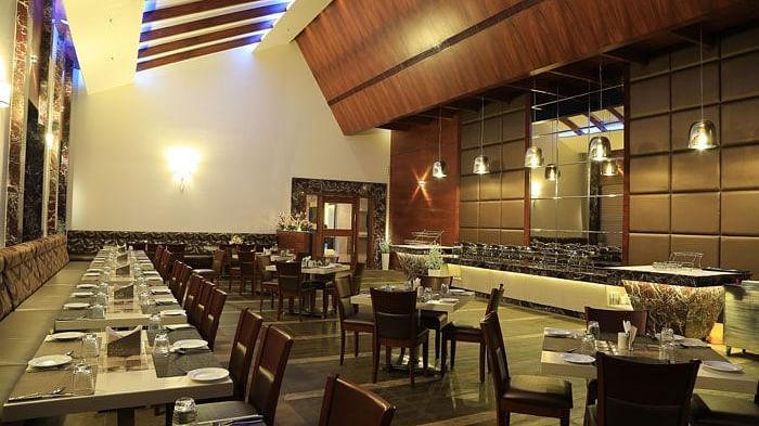 A spacious restaurant with elegant wooden interiors, neatly arranged tables, and a warm ambient lighting design. - Dhanalakshmi Srinivasan Hotels, Perambalur