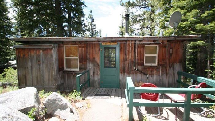 A wooden cabin with a trimmed door and porch sits amidst a dense forest. - Kit Carson Lodge
