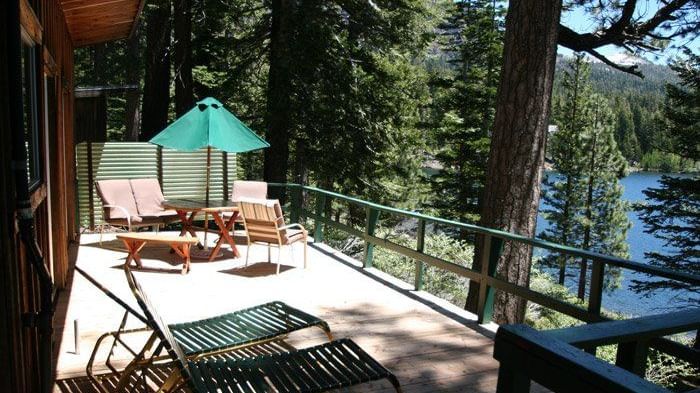 A spacious cabin deck with railings facing a serene lake. - Kit Carson Lodge