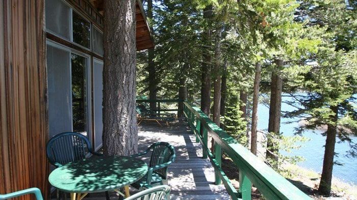 A cabin balcony with  railings offering a serene view of a lake through tall trees. - Kit Carson Lodge