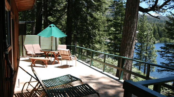 A spacious cabin deck with railings facing a serene lake. - Kit Carson Lodge