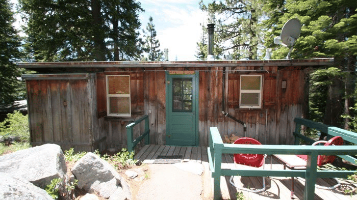 A wooden cabin with a trimmed door and porch sits amidst a dense forest. - Kit Carson Lodge