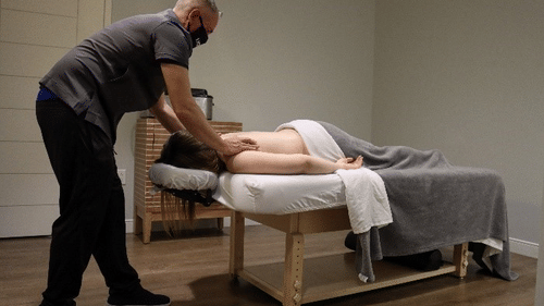 A person is getting a massage from a masked therapist in a well-lit room with a wooden floor at YO1 Longevity & Health Resorts, Catskills