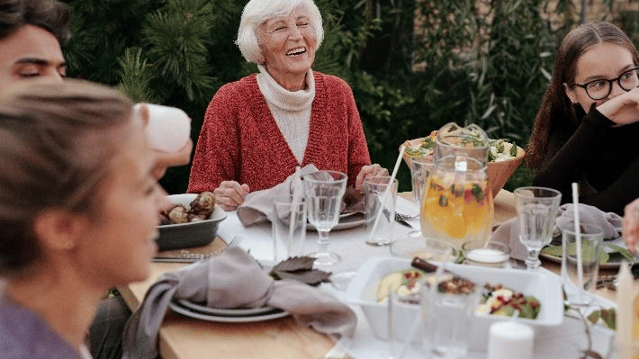 A multigenerational family gathers around an outdoor dining table, enjoying a meal together with laughter, conversation, and delicious food