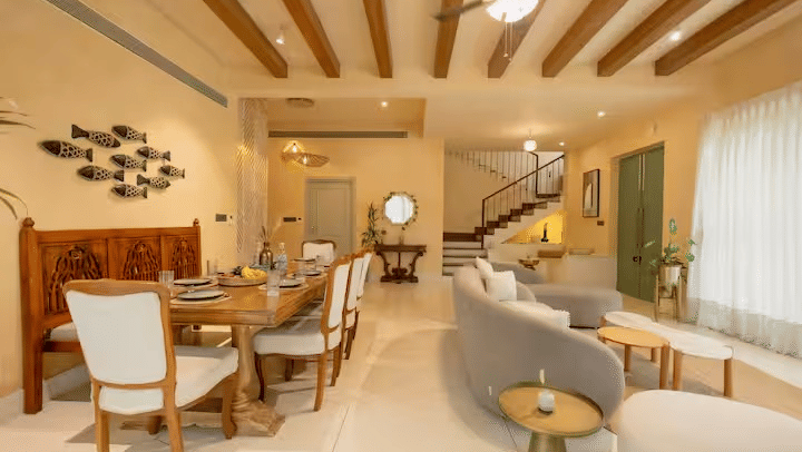 Dining and living area of Lime Tree Hotels & Service Apartment Private Limited featuring a wooden beam ceiling, a dining table, and a curved sofa.