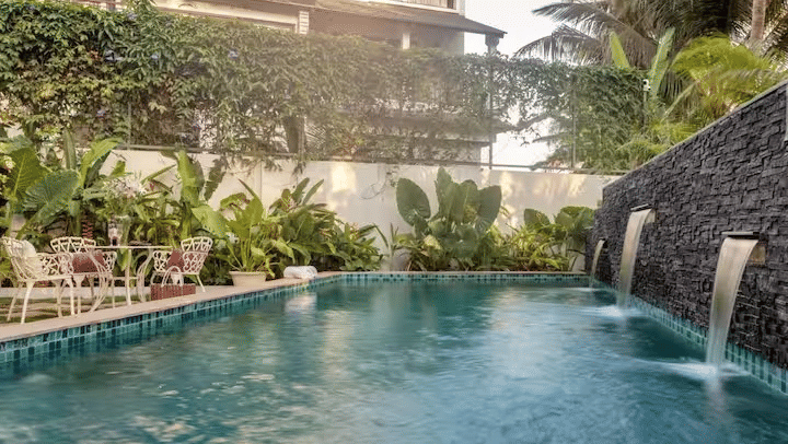 Swimming pool of Lime Tree Hotels & Service Apartment Private Limited featuring a stone waterfall feature, surrounding greenery, and poolside loungers.
