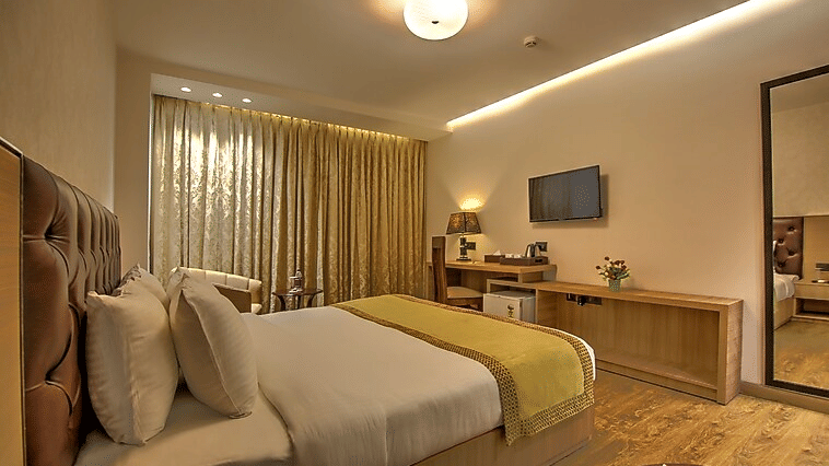 A warm & cosy guest room setup featuring a bed with a gold runner, ambient ceiling lighting, and heavy drapes for privacy - Hotel 91 HUDA City Centre, Gurugram