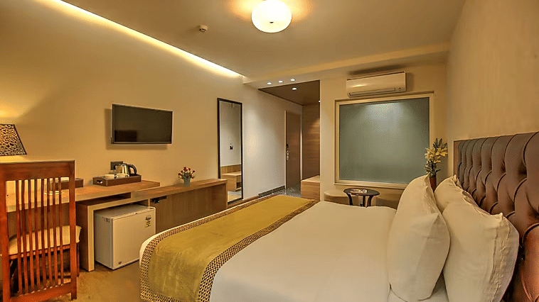 A view of the guest room highlighting the integrated storage units, mini-fridge, and a bed dressed in white linens with a gold-toned runner - Hotel 91 HUDA City Centre, Gurugram