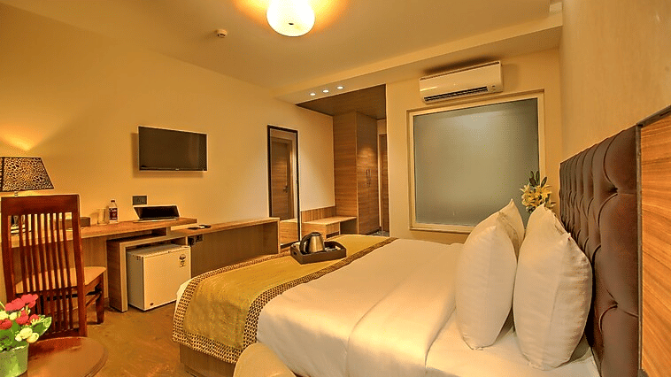 A cosy guest room with warm ambient lighting, featuring a well-made bed, a small refrigerator, and a functional workspace area - Hotel 91 HUDA City Centre, Gurugram