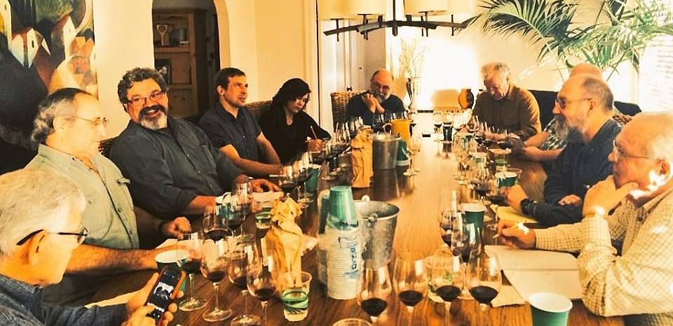 A bunch of people  sitting around a table with glasses and bottles on top of it.