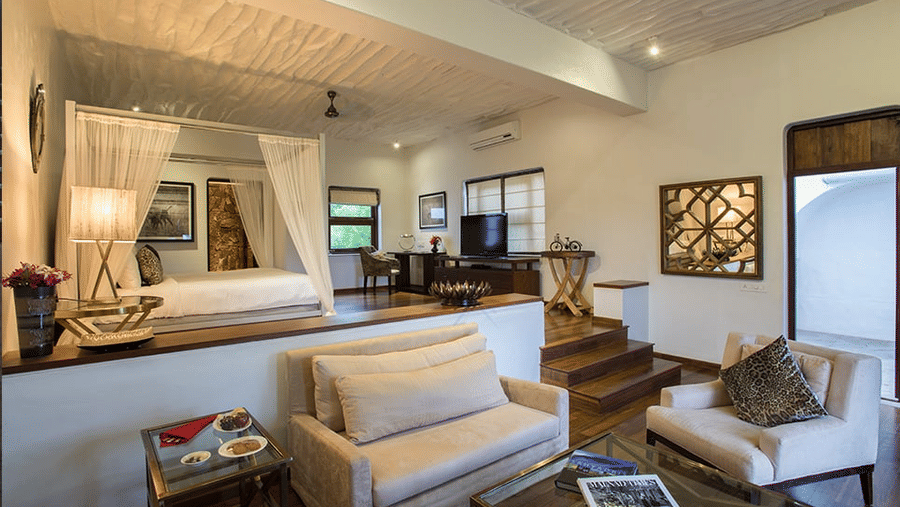 Interior of The Residence at The Serai Bandipur, featuring living space with sofas, table, wall art, and an elevated bed.