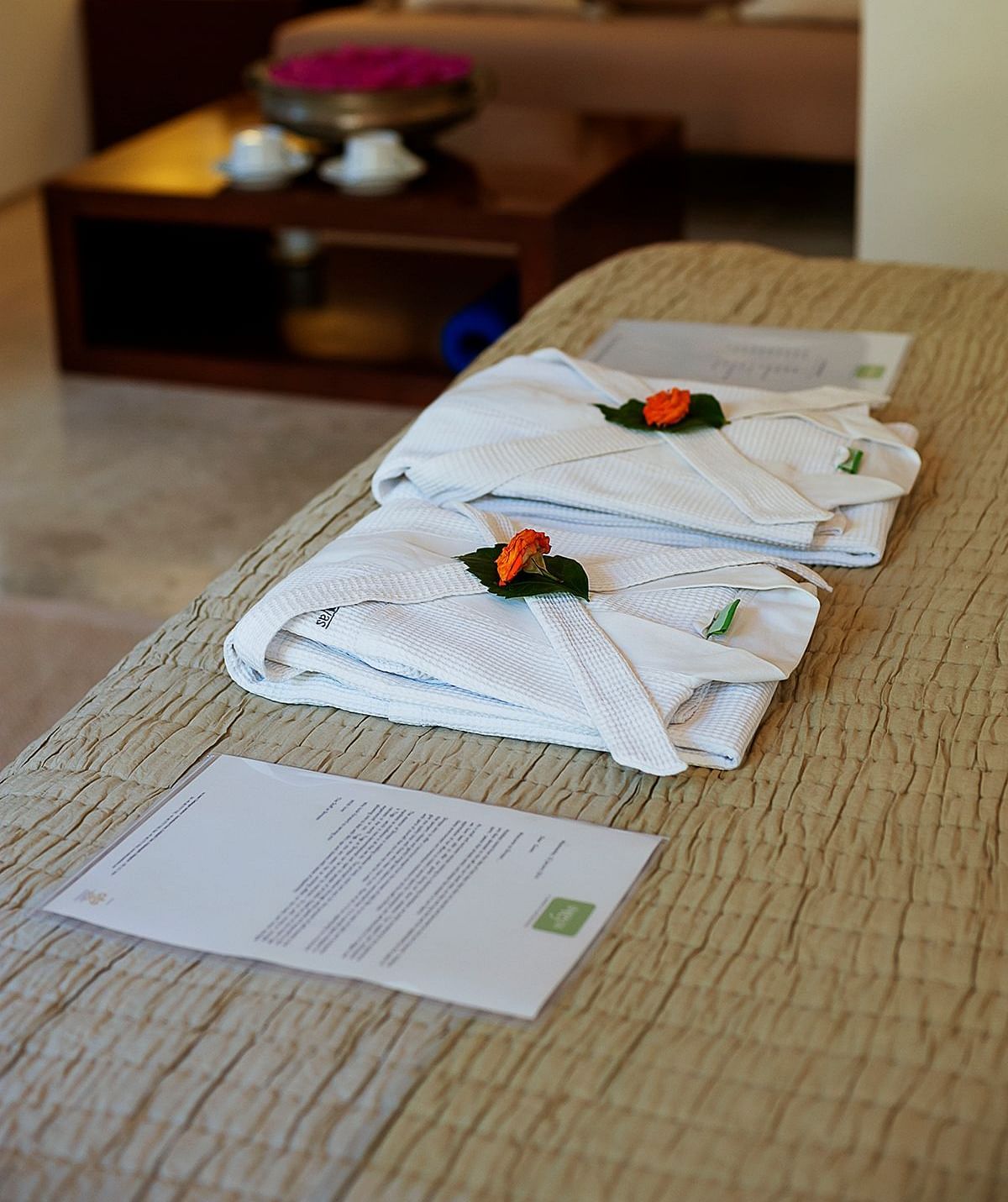 Close-up of towels arranged with flower petals on a bed with a couch in the background - Shreyas Retreat