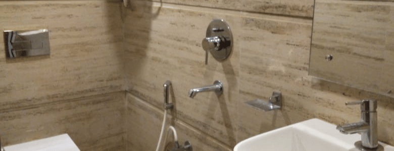 Modern bathroom with light beige tiled walls, a shower, toilet, sink, and a water heater mounted above at Hotel Dolphin Darjeeling.