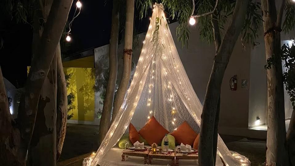 A lit, triangular structure hangs, adorned with string lights, in a dark setting.
