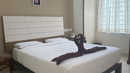 Room with white double bed, window, and air conditioner at Hotel SRM Grands –Chennai.