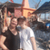 2 people standing together outside an orange temple with a red flag under a clear blue sky.