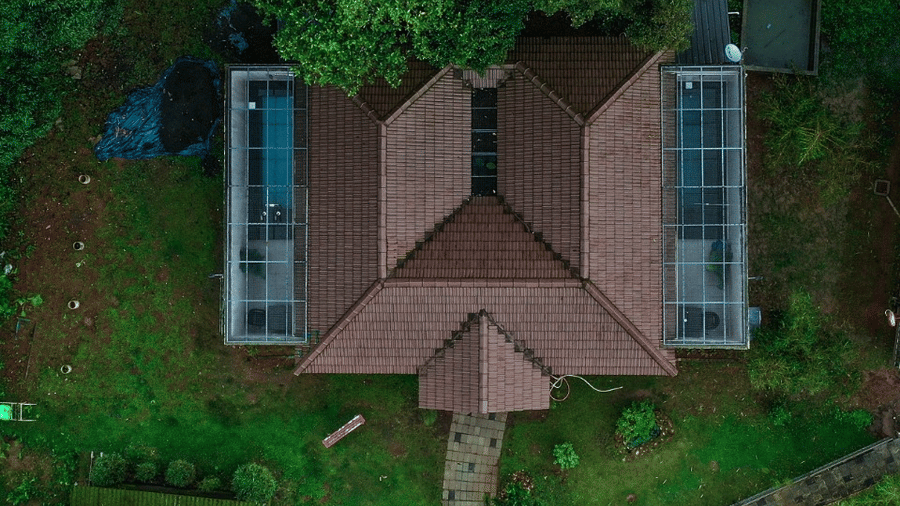 An aerial view shows a building with a distinctive M-shaped roof, surrounded by greenery.- Abad Brookside Lakkidi, Wayanad