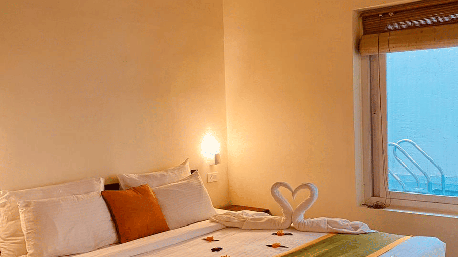A bedroom features a made bed and a window, offering a comfortable space.- Abad Brookside Lakkidi, Wayanad