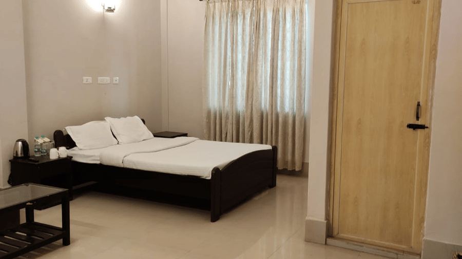 A room at Lake Side Resort Neermahal, fetauring a bed, spreads, pillows, a door, a table, and a window covered in curtains.