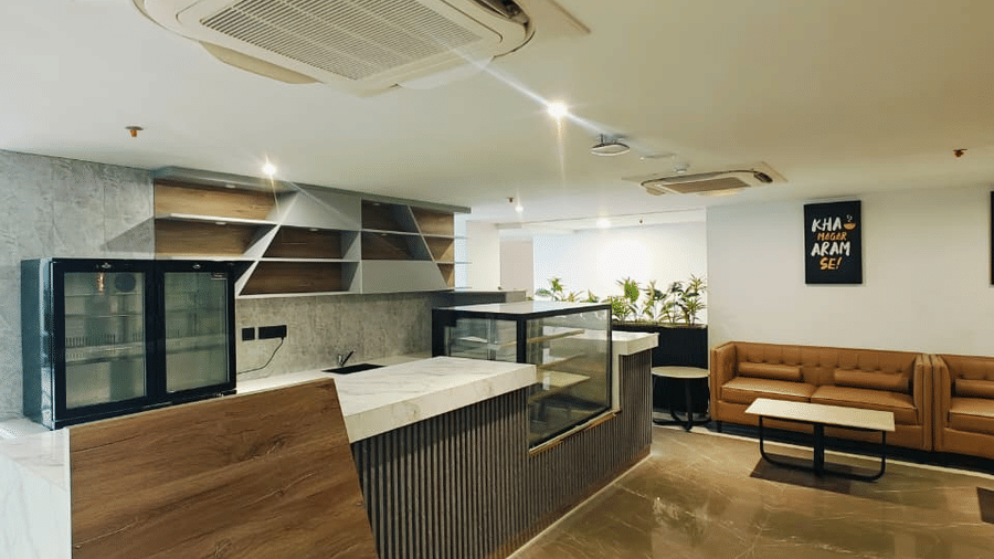 Vertical view of the Mr. Confectioner cafe counter at Pride Premier Greater Noida, highlighting the wooden finishes and overhead air-conditioning units.