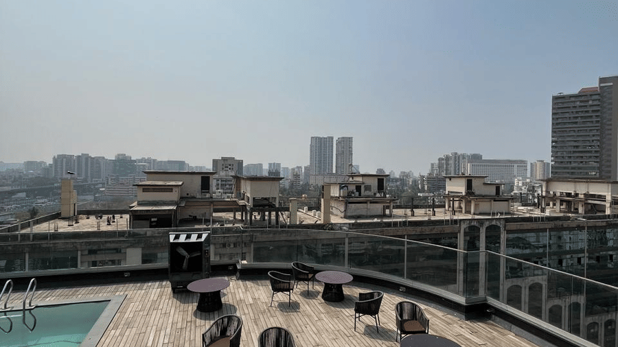 Panoramic high-angle view of a rooftop terrace with small tables and a distant city skyline under a clear sky.