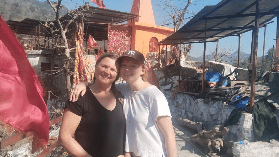 2 people standing together outside an orange temple with a red flag under a clear blue sky.