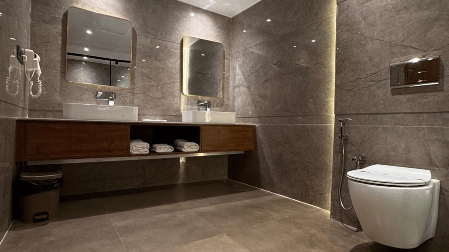 Modern bathroom with gray marble walls, dual sinks on a wooden vanity, wall-mounted toilet, soft recessed lighting, and neatly rolled white towels for a sleek look - Silver Sand Beach Resort, Havelock