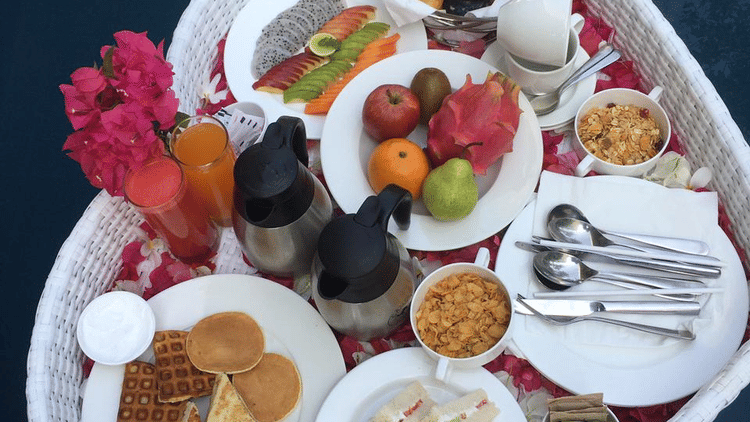 A white heart-shaped floating tray filled with small dishes of fruit salad and breakfast items.