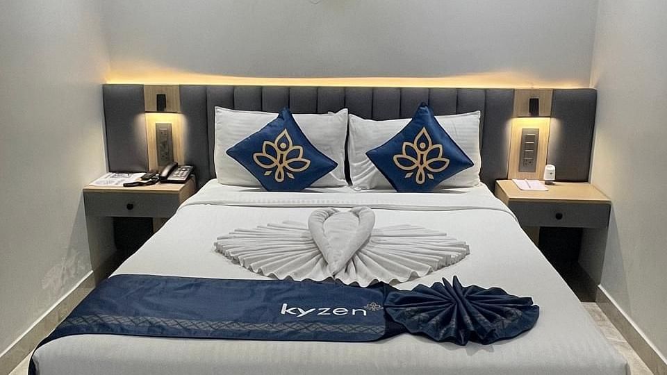 Bed with decorative cushions, side tables, and soft lighting, featuring towel art in the shape of a heart at Hotel Kyzen, Hitech City.