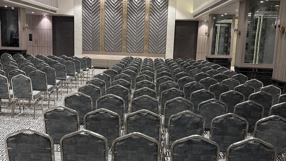 A large room is set up with rows of dark chairs facing a front area - Melior Inn