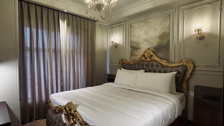 A wide-angle shot of the plush double bed with a regal headboard under a beautiful chandelier at the bedroom of the Presidential Suite of F Hotels, Bengaluru.