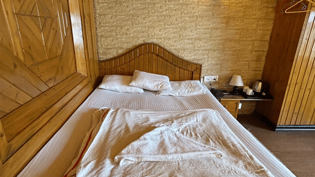 Close-up of a neatly made double bed with light bedding, wooden headboard, and wooden ceiling at Hotel Dolphin Darjeeling.