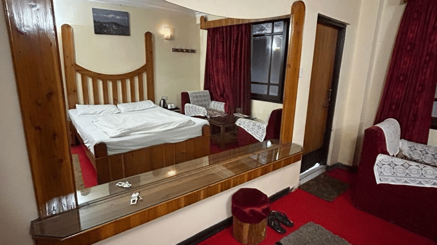 Hotel room featuring a bed with a wooden headboard, a large mirror, red carpet, and a striped rug at Hotel Dolphin Darjeeling.