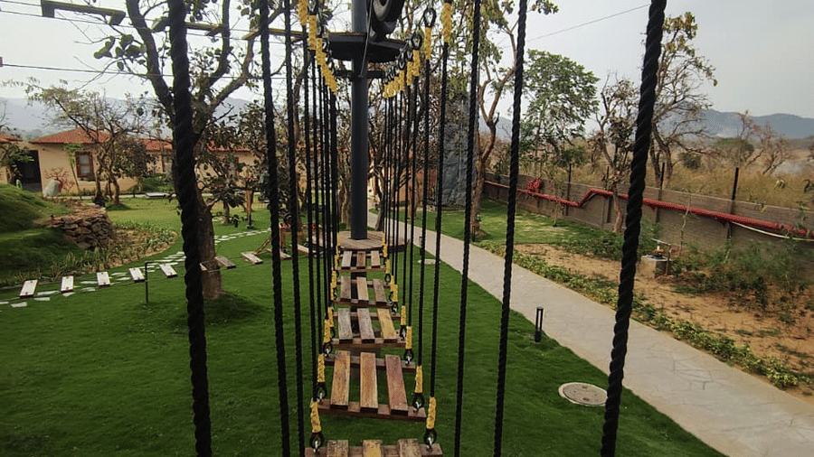 An elevated outdoor course featuring a suspended wooden plank walkway over a green lawn at Hotel Sonar Bangla, Ajodhya Hills.