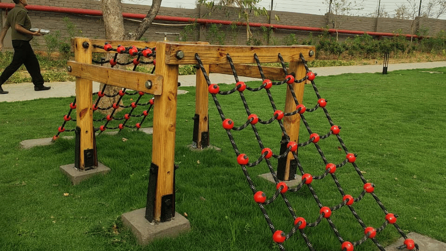 An outdoor obstacle featuring a wooden A-frame structure with a red rope climbing net on a lawn at Hotel Sonar Bangla, Ajodhya Hills.