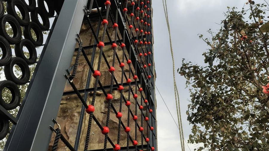 A tall metal tower featuring a large climbing net constructed of black ropes with red joints at Hotel Sonar Bangla, Ajodhya Hills.
