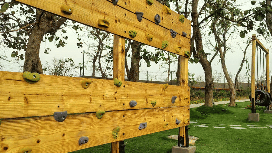 A grassy outdoor area featuring a freestanding wooden climbing wall with colourful holds at Hotel Sonar Bangla, Ajodhya Hills.