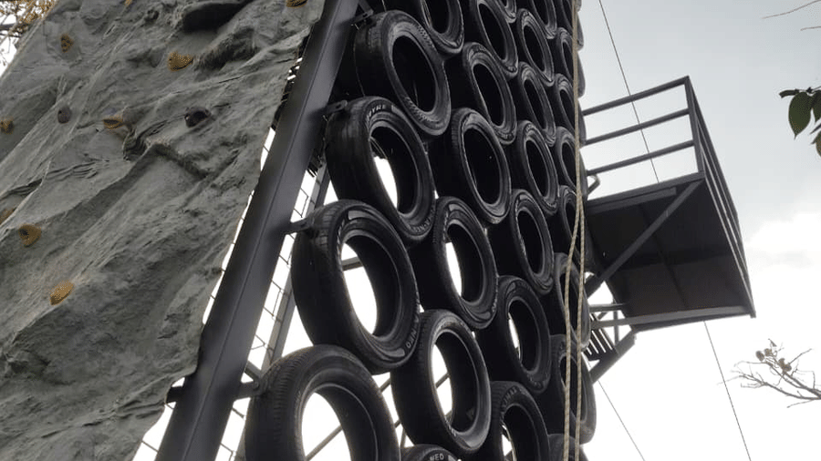 A tall outdoor structure featuring a textured climbing wall next to a column of stacked black tyres at Hotel Sonar Bangla, Ajodhya Hills.