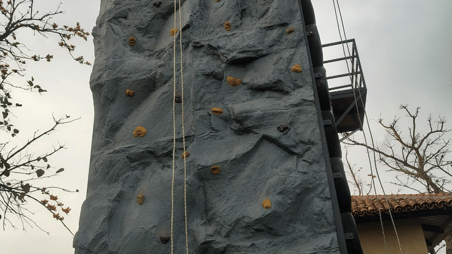 A tall metal structure featuring a grey artificial rock climbing wall with scattered holds at Hotel Sonar Bangla, Ajodhya Hills.