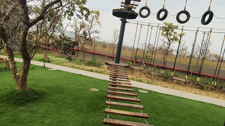 An outdoor activity area featuring a suspended wooden plank bridge over a lawn with trees at Hotel Sonar Bangla, Ajodhya Hills.