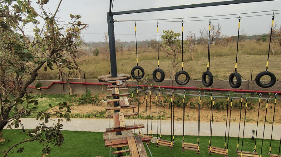 An outdoor activity area featuring a suspended rope bridge with wooden planks above a green lawn at Hotel Sonar Bangla, Ajodhya Hills.