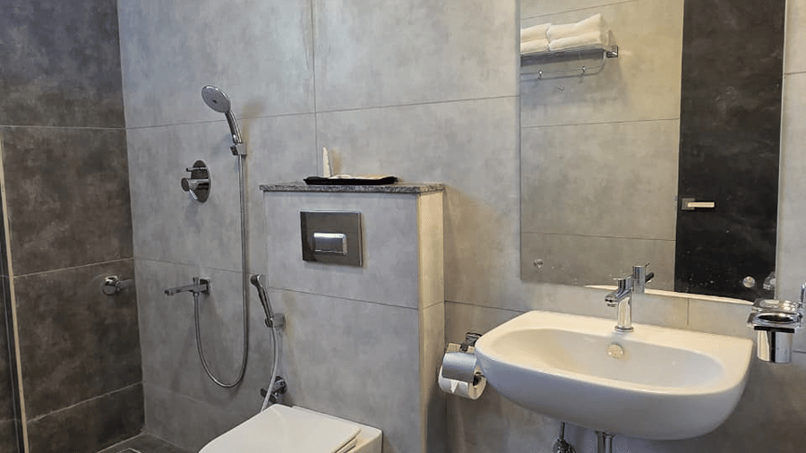 A bathroom with dark tiled walls, a wash basin, mirror, and toilet fitted along the side.